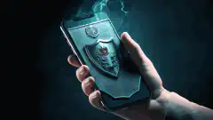  Un escudo con el símbolo de un candado protege un teléfono móvil de la mano de un hacker que intenta acceder a él.